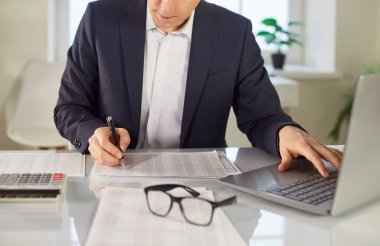 İş yerindeki mali belgelerle masa başında çalışan takım elbiseli genç bir muhasebeci. Şirket çalışanı dizüstü bilgisayarla masada oturmuş şirket denetimi yapıyor. Muhasebe işi kavramı.