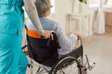 Hemşire ya da üniformalı bir sağlık görevlisi tıbbi klinikte tekerlekli sandalyedeki engelli bir kadını itiyor. Huzurevinde özürlü bir kadın. Rehabilitasyon ve bakıcı destek kavramı.