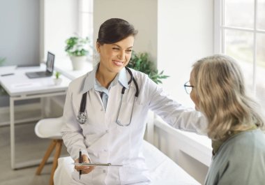 Tıp kurumlarında nezaket ve destek. Doktor, hastasıyla sıcak bir konuşma yapıyor ve onu olumlu yönüne oturtarak neşelendiriyor. Doktor olgun bir kadının omzuna cesaret verici bir el koydu..