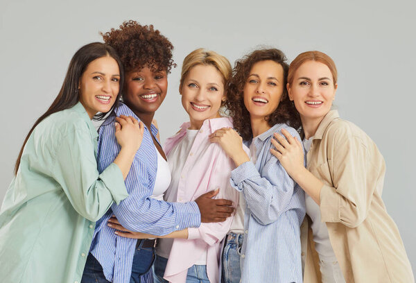 Group portrait of five happy diverse women standing close together, hugging and smiling at camera. Cheerful multiracial female friends in casual outfits embracing, showing unity and friendship.