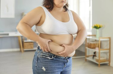 Şişman karnından deri tutan, kilo vermeye çalışan, obeziteden muzdarip, dengeli beslenme ihtiyacından muzdarip şişman bir kadının kesilip biçilmiş görüntüsü.