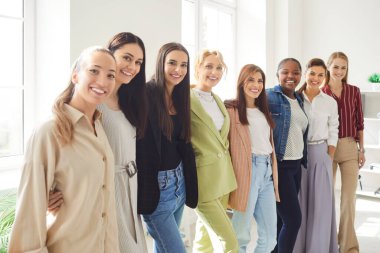 Neşeli, genç, çeşitli kadın iş arkadaşları ve günlük kıyafetler giyen şirket çalışanlarından oluşan bir grup ofiste sırada sıralanmış kameraya güvenle bakıyor. İş adamları portresi.