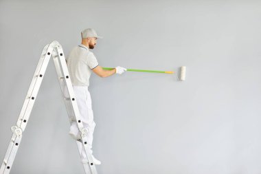 Merdivende boya fırçası olan erkek ressam, inşaat işçisi, üniforma giyen profesyonel servis elemanı, oda tamiri işlerini bitiren ev dekorasyonundan sonra dairedeki renk duvarı.