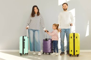 Aile gezgini, anne-baba, kız çocuğu, tekerleğin yanında duran parlak bavullar, yaz tatili için hazır, valiz çantası seyahati, bavul yolculuğuna giysi, taşınma planı