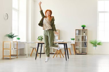 İyi bir işten sonra evde ya da ofiste zıplayan mutlu, sıradan kıyafetler giyen genç bir kızın tam vücut fotoğrafı. Güzel bir kadın tatmin olmuş bir yüz ifadesiyle eğleniyor. İnsan duyguları kavramı.