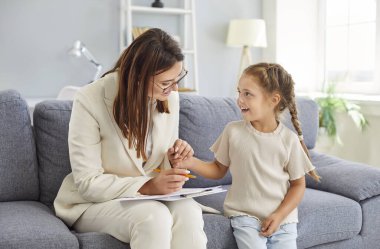 Sevecen, neşeli kadın psikolog kadın terapi seansı sırasında koltukta ya da ofiste oturan sevimli, gülümseyen bir çocuk hastayla konuşuyor. Ruh sağlığı ve çocuk psikolojisi kavramı.
