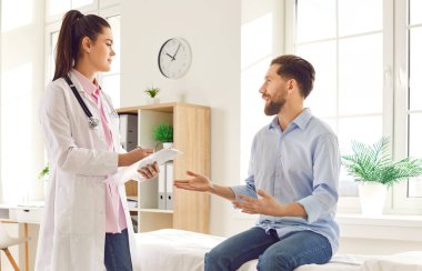 Kadın doktor, muayenehanedeki danışman erkek hasta semptomları tanımlıyor, iyi laboratuvar sonuçlarını paylaşıyor, Mutlu adam kliniğe gidiyor, tıbbi bakım alıyor, sağlık tavsiyesi alıyor, tedavi planını tartışıyor.