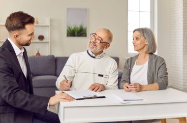 Gri saçlı yaşlı çift emeklilik sigortası hakkında finans danışmanıyla konuşuyor. Yaşlı adam ve kadın danışman ile bir araya gelerek yatırım sözleşmesi imzalayacaklar..