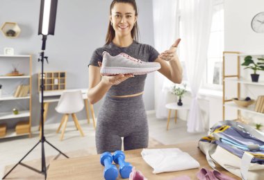 Sportif genç kadın fitness modeli blogcusu ticari sosyal medya pazarlama işbirliği spor ayakkabıları markası ile bütünleşme, promosyon videosu çekme, kamera önünde ayakkabı tutma ve gösterme