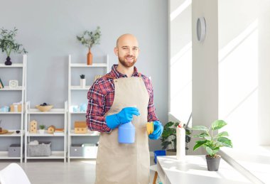 Ev işleri yapan mutlu bir adamın portresi, ev temizliği ya da mobilya temizliği, evi temizlemek ve kameraya gülümsemek. Davranış, evi temiz ve düzenli tutmanın memnuniyetini yansıtır..