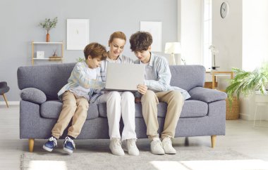 Anne ve iki oğlu kanepede dizüstü bilgisayarla oturuyorlar, yakın plan. Mutlu gençler anneleriyle evde vakit geçirirler. Çevrimiçi aile alışverişi kavramı, internette çocukların güvenliği.
