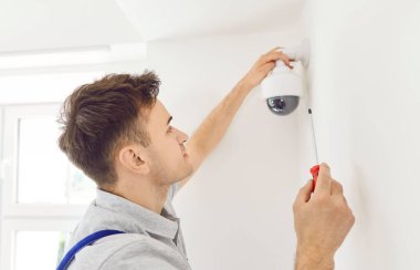 Üniformalı genç bir teknisyenin portresi. Kapıya güvenlik kamerası yerleştiriyor. Modern ofiste ya da evde güvenlik kameralarını tamir ederken erkek işçi tornavida kullanıyor.