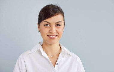 Resmi beyaz gömlekli, güler yüzlü genç bir girişimcinin portresi. Gri stüdyo arka planında, fotokopi alanı ile izole edilmiş ve kameraya neşeli görünüyor. İş portresi kavramı