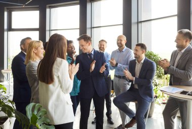İş dünyası ekibi ofisteki bir toplantıda başarıyı alkışlıyor ve kutluyor. İş ortamında işbirliği, takım çalışması ve profesyonel başarı, ortak başarılarının altını çiziyor.