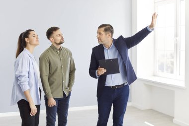 Emlakçı genç bir çifte ev gösteriyor, yakın plan. Boş bir dairede bir iş adamını dinleyen bir aile. Yeni ev, emlak komisyoncusu, ipotek anlaşması, yatırım