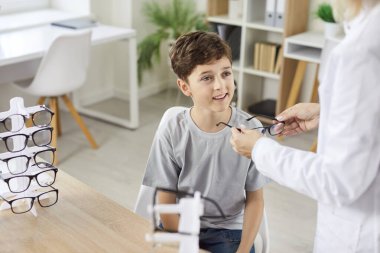 Göz doktorunun ya da göz doktorunun çocuk hastaya görme yetisini geliştirmek için yeni gözlük vermesi. Göz doktoru kliniğinde ya da optik mağazada gözlük seçen küçük bir çocuk. Oftalmoloji, göz sağlığı..