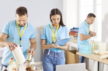 Gönüllüler, gıda paketlerinin insani yardım merkezinde kutulara doldurulmasında işbirliği yapıyorlar. Takım çalışması, yardım ve yardımın temel bağışların sağlanmasında taşıdığı önemi vurguluyor.