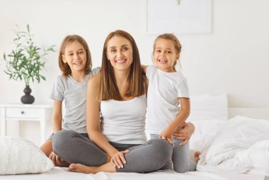 Mutlu gülümseyen iki çocuklu bir annenin portresi. Sabahları yatak odasında oturmuş birlikte vakit geçirmekten zevk alan kameralara bakıyor. Aile ve anneler günü konsepti