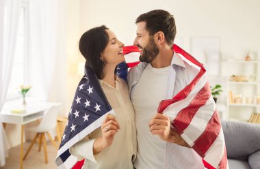 Mutlu ve gülümseyen aile çifti evde Bağımsızlık Günü 'nü kutluyor, Amerikan bayrağıyla kucaklaşıyorlar. Vatanseverlik anı, ABD vatandaşlığının paylaşılan birlikteliği, sevgisini ve gururunu vurguluyor.