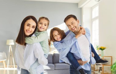 Dört kişilik mutlu bir ailenin portresi evde birlikte eğleniyor. Gülümseyen ebeveynler oturma odasındaki neşeli çocuklarına binip oyun oynuyorlar ve eğleniyorlar. Aile ve çocukluk kavramı.