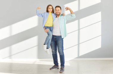 Mutlu, genç, gülümseyen bir baba, küçük oğlunu elleriyle tutarak güç ve güç gösterisi yapıyor. Baba ve oğlu kameraya bakıyor. Babalar günü ve babalık kavramı..