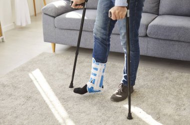 İyileşme sürecinde koltuk değnekleriyle yürüyen kırık bacaklı bir adamın orta bölüm çekimi. Rehabilitasyon, tıbbi bakım ve yaralanma ve travmanın yönetiminde esneklik.