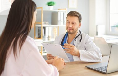 Doktor bir hastayla görüşüyor. Elinde dosya olan bir erkek doktor masasında kadın bir hastayla oturuyor. Beyaz önlüklü bir adam muayenehanede bir kadınla konuşuyor. Sağlık hizmetleri, doktor konseptini ziyaret