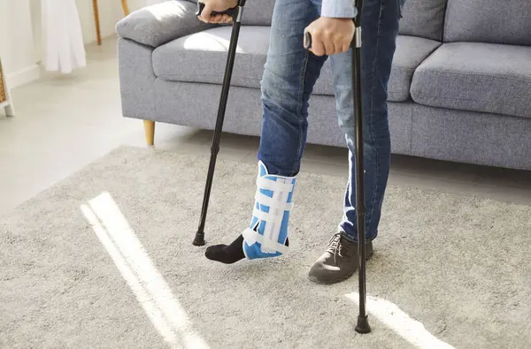 İyileşme sürecinde koltuk değnekleriyle yürüyen kırık bacaklı bir adamın orta bölüm çekimi. Rehabilitasyon, tıbbi bakım ve yaralanma ve travmanın yönetiminde esneklik.