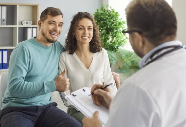 Mutlu genç adam sağlık kliniğinde karısının hamilelik planladığını gösteren tabela gösteriyor. Hastanedeki aile doktoru terapistiyle görüşen bir çift. Sağlık ve Tıp Konsepti.