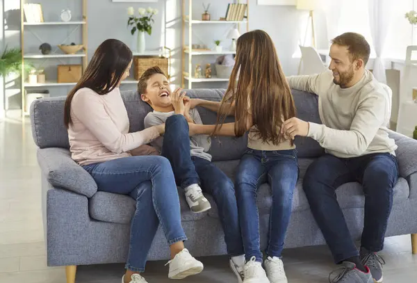 Mutlu ebeveynler ve çocuklar eğleniyor ve birbirlerini gıdıklıyorlar, gülüyorlar ve evde birlikte vakit geçirirken pozitif duygularını ifade ediyorlar, koltukta poz veriyorlar. Neşeli anne, baba, oğul ve kız