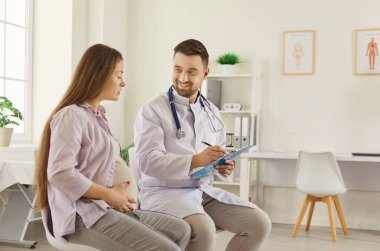 Genç hamile bir kadın klinikte doktor ziyareti, erkek jinekolog danışman anne, doğum öncesi sağlık, sağlıklı hamilelik, doğum öncesi muayenesi, profesyonel doğum öncesi bakım.