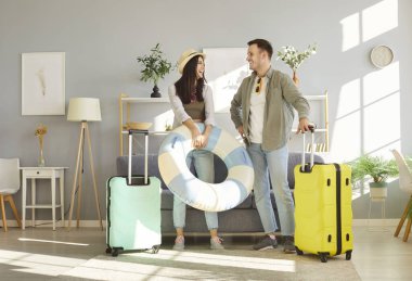 Evdeki oturma odasında bavullarıyla tatil gezisi için hazır bekleyen mutlu ve genç bir çift. Tatil, seyahat ve yaz yolculuğu konsepti.