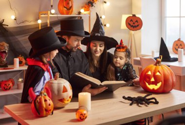 Genç anne evde Cadılar Bayramı partisini kutlamak için maskeli balo kostümleriyle oturma odasında oturan çocuklar için kitapta korkunç bir hikaye okuyor. Aile kutlama konsepti.