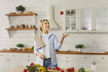 Mutlu ev hanımı sebzelerle hokkabazlık yapıyor, organik taze vejetaryen salatası hazırlıyor, mutfak içlerine karşı poz veriyor, aile için akşam yemeği hazırlıyor, dengeli beslenmeye devam ediyor.