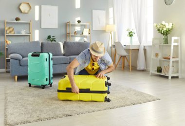 Mutlu gülümseyen adam oturma odasında oturmuş yaz tatiline hazır bavullarını topluyor. Neşeli erkek turist tatile çıkıyor. Seyahat, seyahat ve yaz konsepti.