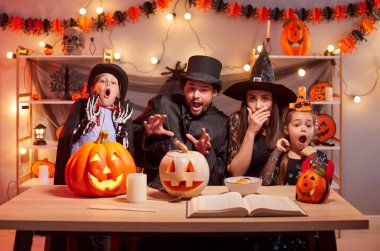 Çocuklu bir aile, korkmuş görünüyor, Cadılar Bayramı partisini evde veriyor, balkabağı süslemeleriyle birlikte eğlence ve heyecan dolu neşeli ve ürkütücü bir atmosfer için kutluyorlar..