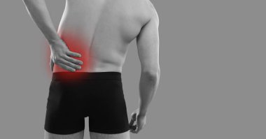 Sol tarafında acı çeken bir adam. İç çamaşırlı hasta, gri arka planda duruyor, iltihaplı sırtına el ele tutuşuyor, kırmızı röfleli, arkadan arkaya bakıyor. Sırt ağrısı kavramı