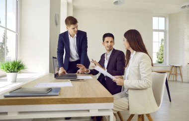 Ofiste çalışan iş ekibi. Bir ofis masasında oturan, belgelerle çalışan bir grup genç bir şeyi tartışıyor ve dizüstü bilgisayar kullanıyor.