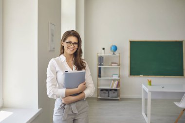 Okula dönelim. Okulda gözlüklü, not defteriyle ayakta duran pozitif öğretmen kadın. Ebeveynlik eğitimi almak.