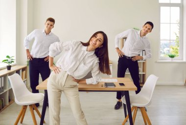 Ofiste spor antrenmanı yapan mutlu iş adamları. Üç kişilik bir grup şirket çalışanı birlikte fitness egzersizi yapıyor. Mutlu genç kadın ve iki erkek yan eğilme egzersizi yapıyor.