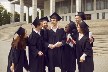 Mezuniyeti kutlayan ve eğlenen çeşitli üniversite öğrencileri. Verandanın önünde dikilen siyah cüppeli, çok ırklı, pozitif arkadaşlar grubu.