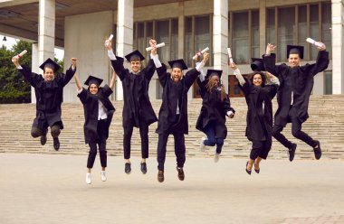 Mutlu öğrenciler mezuniyet törenine seviniyor ve diplomaları ellerinde tutarak zıplıyorlar. Üniversite geçmişinde siyah cüppeli ve şapkalı çok ırklı erkek ve kızların portresi. Mezuniyet konsepti.