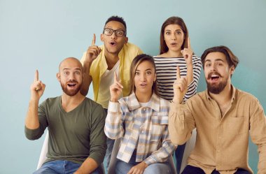 Bir grup çok ırklı genç açık mavi arkaplanı işaret eden fikirler üretiyor. Sancak arka planında günlük giysiler içinde duygusal neşeli insanlar. Fikir kavramı veya yaratıcı anlayış
