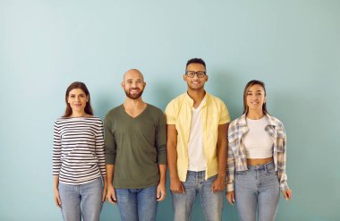 Mutlu gençlik grubunun portresi. Genç, melez, çok ırklı, gündelik kıyafetler giyen, kameraya bakan ve mavi stüdyonun arka planında sıralanmış gülümseyen insanlardan oluşan bir ekip.