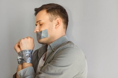 Gri zeminde elleri bağlı ve ağzı bantlı bir şekilde yatan bir adam, suçu, adam kaçırmayı ve şiddeti tasvir ediyor. Tehlike, istismar ve zorla alıkoyma ve zorla alıkoyma gibi ciddi sorunlar..