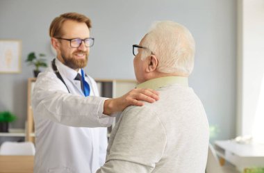 Klinikteki sağlık muayenesinde yaşlı, kır saçlı bir adamın portresi. Erkek doktor ya da hemşire kıdemli hastasına destek oluyor. İlaç ve sağlık hizmetleri kavramı.
