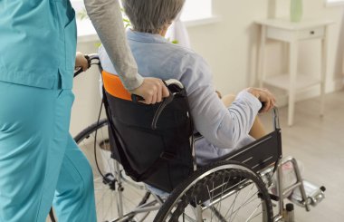 Ciddi bir yaralanmadan sonra klinikte tedavi ve rehabilitasyon gören hemşire tarafından tekerlekli sandalyedeki tanınmayan yaşlı kadının kırpılmış görüntüsü. Yaşlılara bakım kavramı