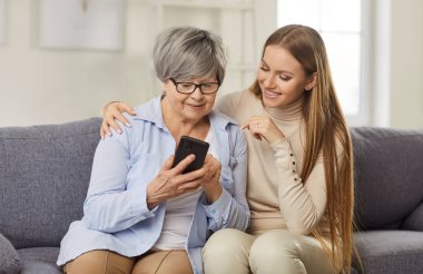 Yaşlı anne elinde yeni akıllı telefonuyla poz veriyor. Yetişkin kızıyla birlikte. İnternetten alışveriş yapıyor ya da video görüşmesi yapıyor. Yaşlılar modern teknolojiyi kolayca kullanıyor.
