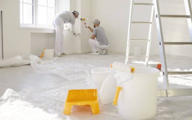 İki kişilik inşaat işçisi ekibi duvarları boya ile boyuyor, evi onarıyor ya da yeniliyorlar, boş odada ekipmanlarla poz veriyorlar, iç tasarım üzerinde çalışıyorlar. 