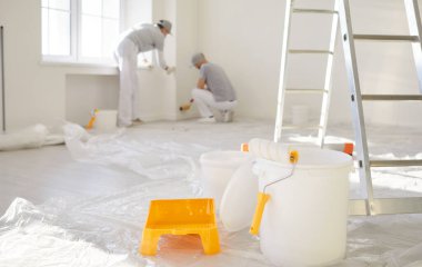 Profesyonel ressamlardan oluşan bir ekip duvarları boyamak için çalışırken, ev yenileme çalışmaları sırasında yerde kova ve boya fırçası bulundu. Yenileme, takım çalışması ve yenileme yoluyla dönüşüm..
